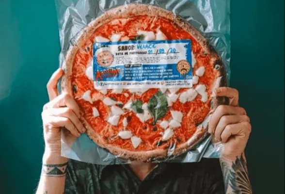 Um homem tatuado cobrindo o rosto com uma pizza embalada a vaco